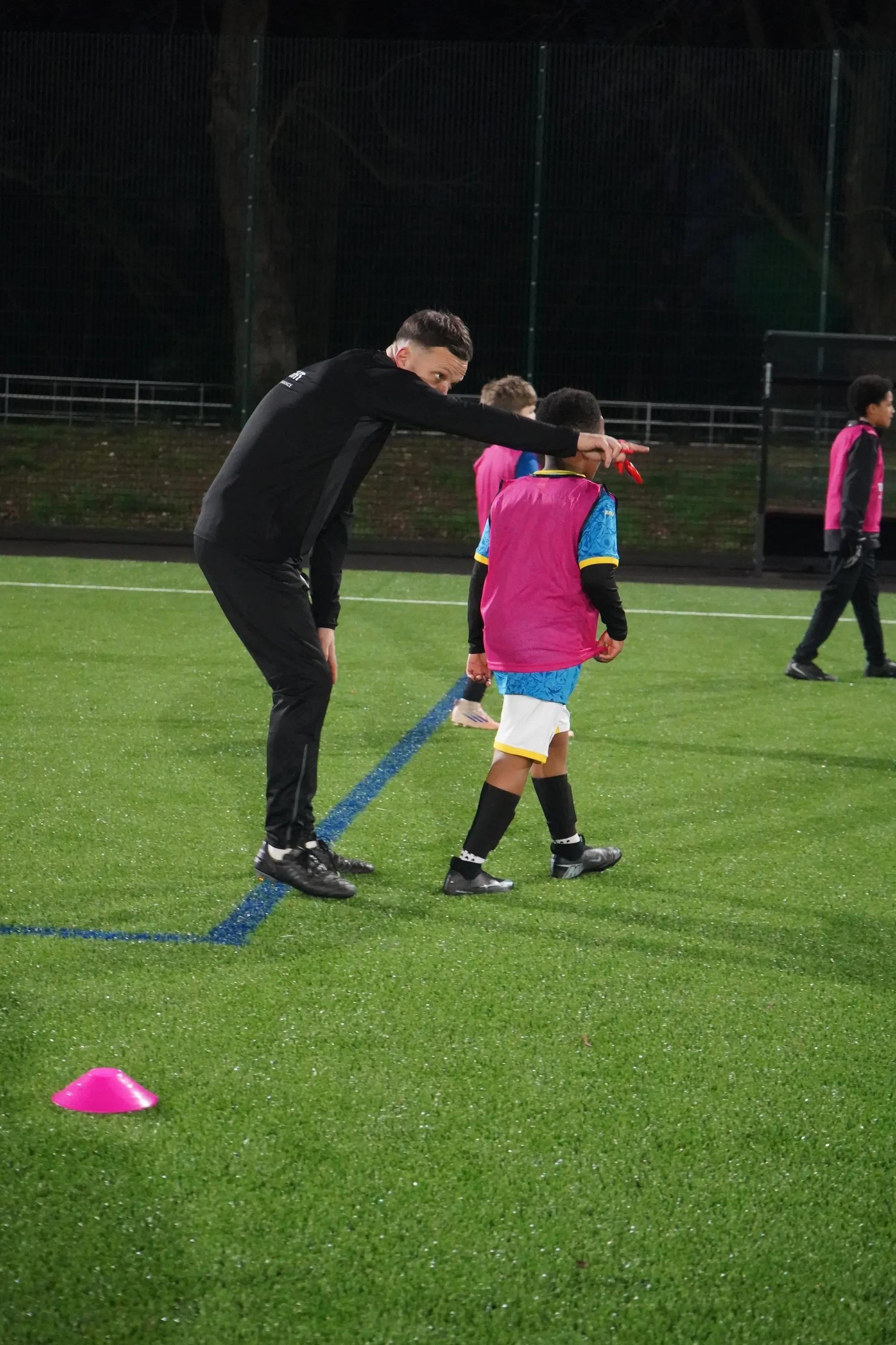 A coach pointing and directing young players during a floodlit TouchTight training session